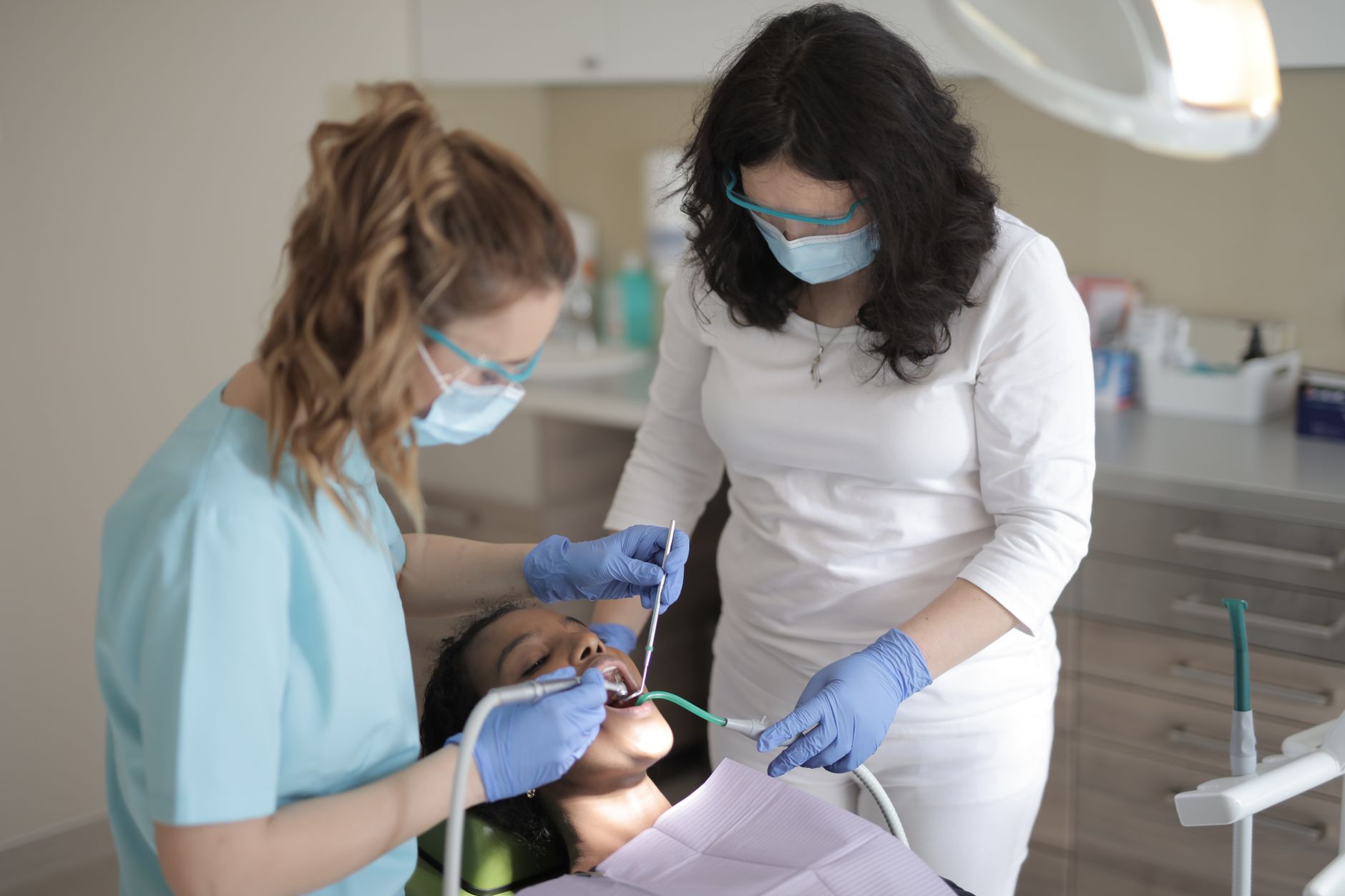 Dos profesionales dentales con mascarilla atendiendo a una paciente en el sillón