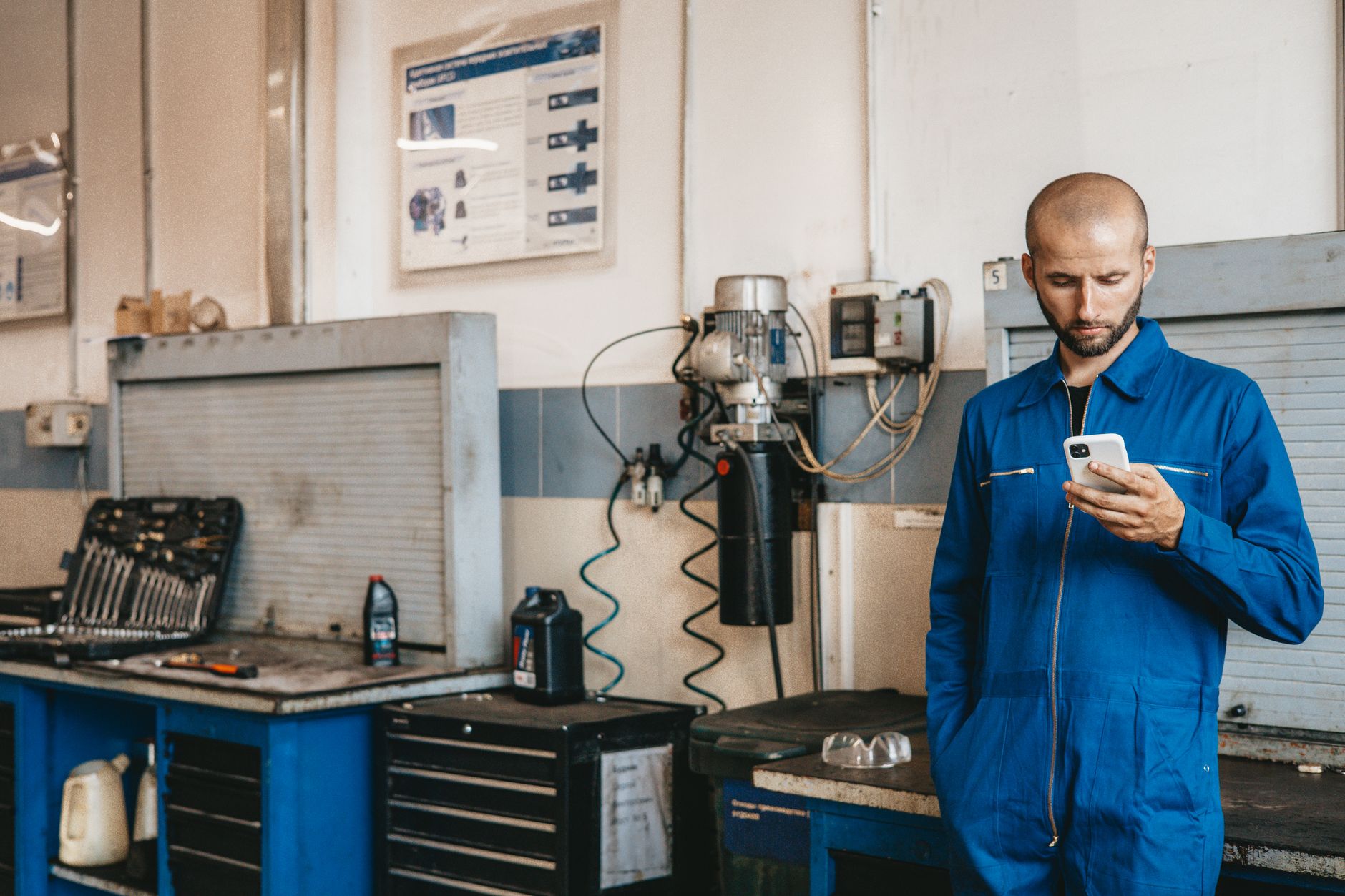 Mecánico con overol azul usando su teléfono para documentar la inspección del vehículo
